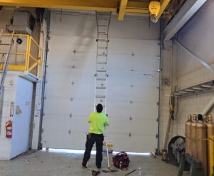 Proactive Garage Door Repair technician repairing a tall commercial sectional door